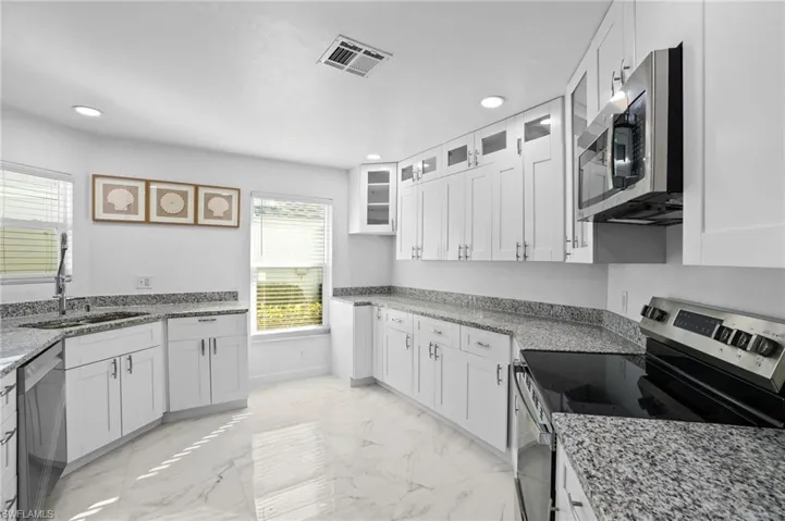 Kitchen featuring appliances with stainless steel finishes, light stone countertops, glass insert cabinets, light marble finish flooring, and recessed lighting