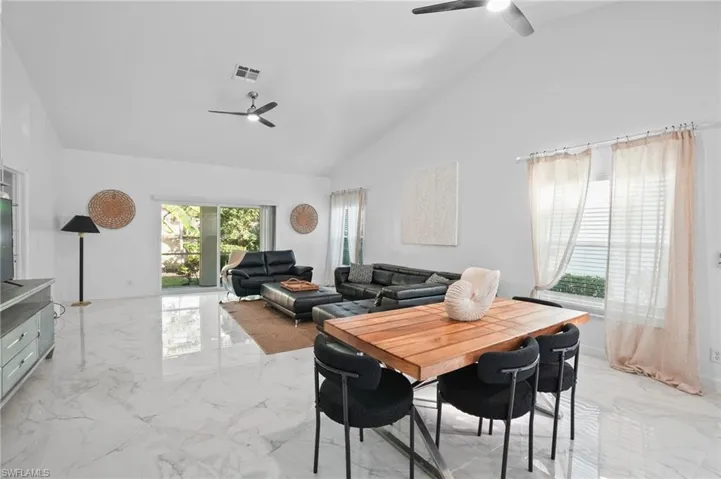 Dining room with high vaulted ceiling, light marble finish flooring, and a ceiling fan