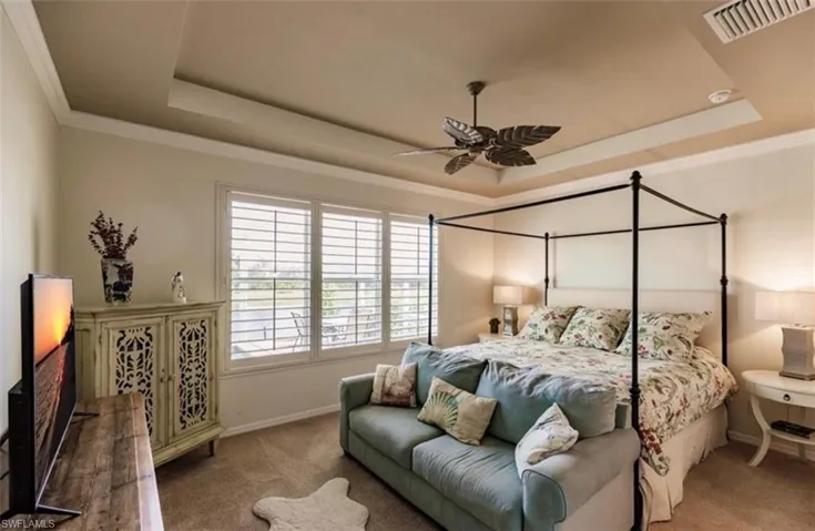 Carpeted bedroom with a tray ceiling, crown molding, and ceiling fan