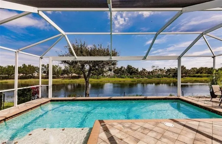 View of pool with glass enclosure, a patio, and a water view