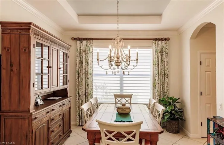 Dining room featuring a notable chandelier, a raised ceiling, crown molding, and light tile patterned flooring