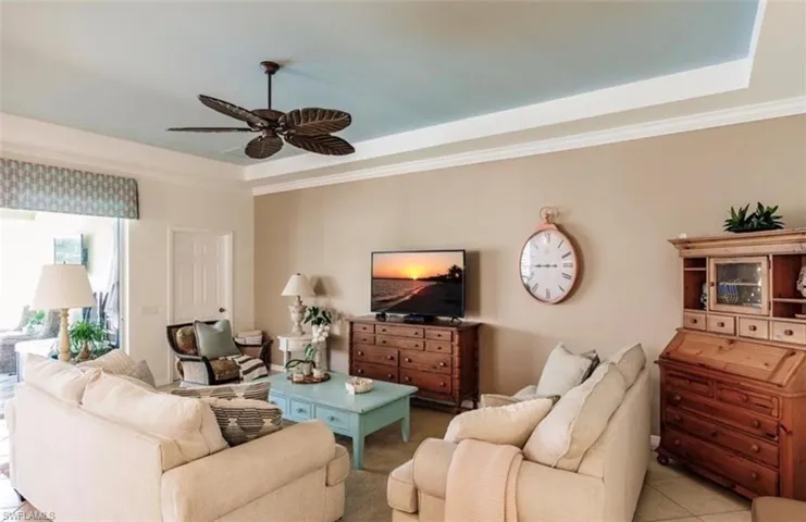 Living room featuring ceiling fan, light tile patterned floors, a raised ceiling, and crown molding