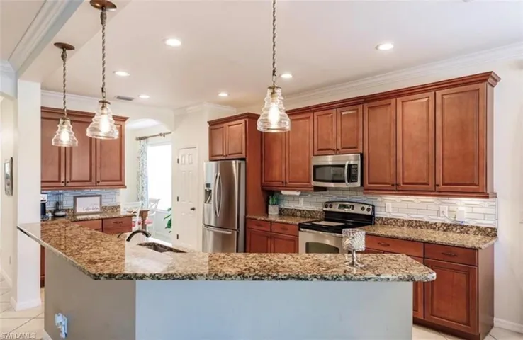 Kitchen with hanging light fixtures, crown molding, light stone countertops, stainless steel appliances, and sink