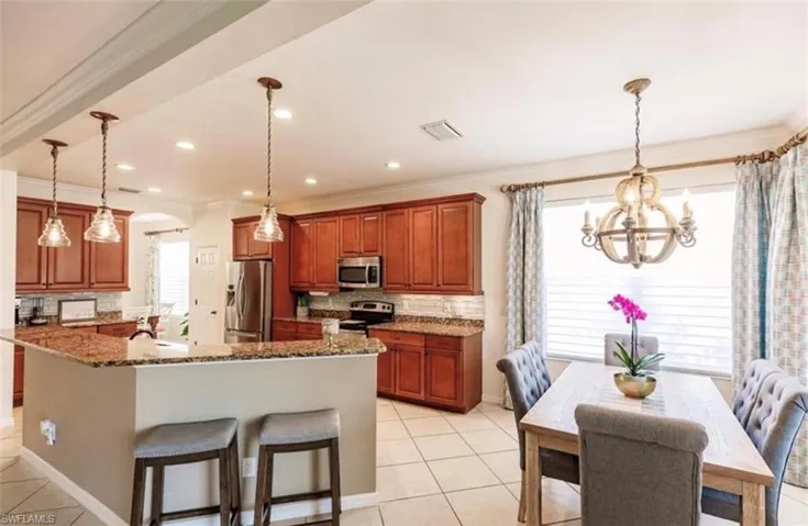 Kitchen with crown molding, decorative light fixtures, stainless steel appliances, dark stone counters, and a breakfast bar area