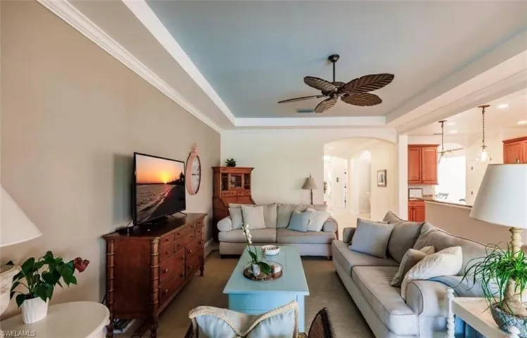 Living room featuring ornamental molding, ceiling fan, dark colored carpet, and a tray ceiling