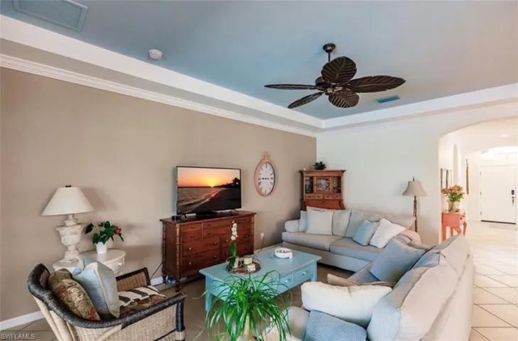 Tiled living room with crown molding, a raised ceiling, and ceiling fan