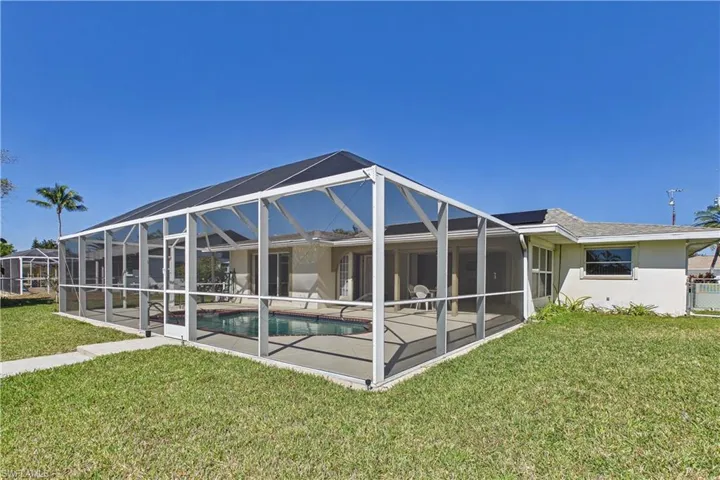 Back of property with a lawn, stucco siding, a sunroom, a lanai, and an outdoor pool