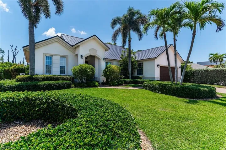 View of front of house with stucco siding, metal roof, a garage, and a front lawn