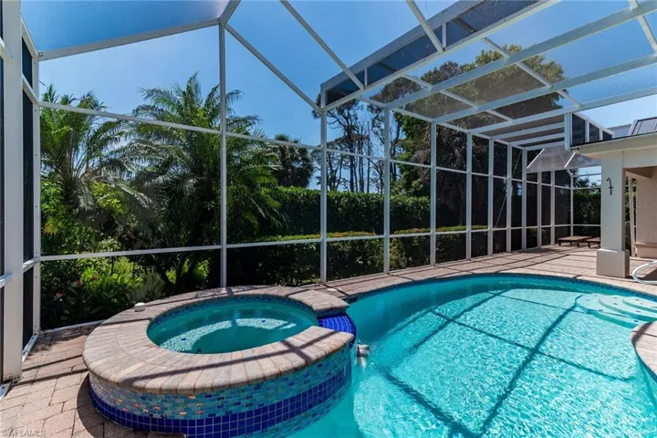 View of pool featuring glass enclosure, a pool with connected hot tub, and a patio area
