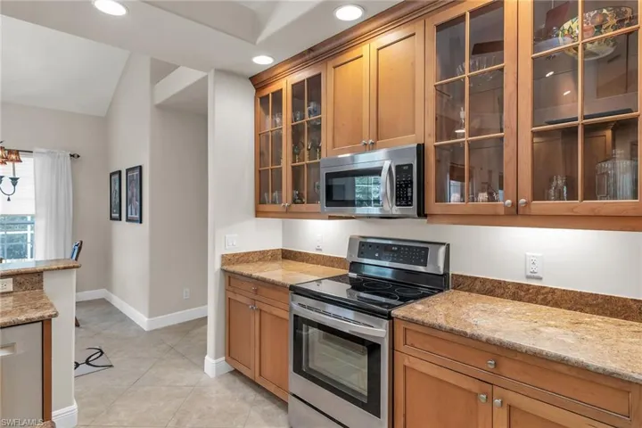 Kitchen featuring glass insert cabinets, light stone countertops, appliances with stainless steel finishes, and brown cabinetry