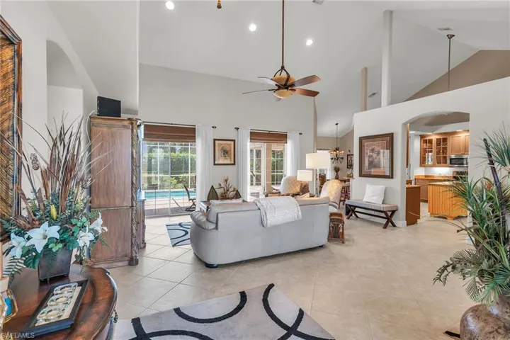 Living area with light tile patterned floors, arched walkways, high vaulted ceiling, and a ceiling fan