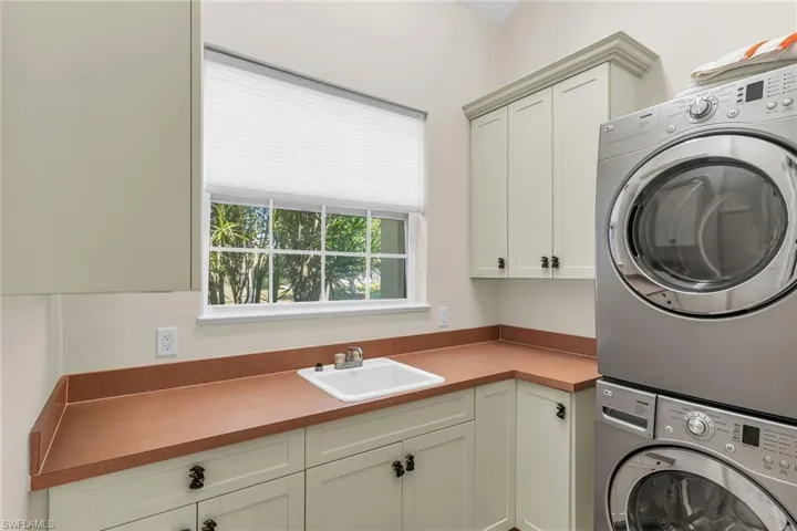Laundry room with cabinet space, stacked washer / dryer, and a sink
