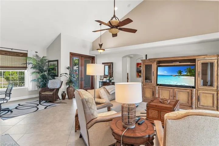 Living area featuring light tile patterned flooring, high vaulted ceiling, baseboards, arched walkways, and ceiling fan