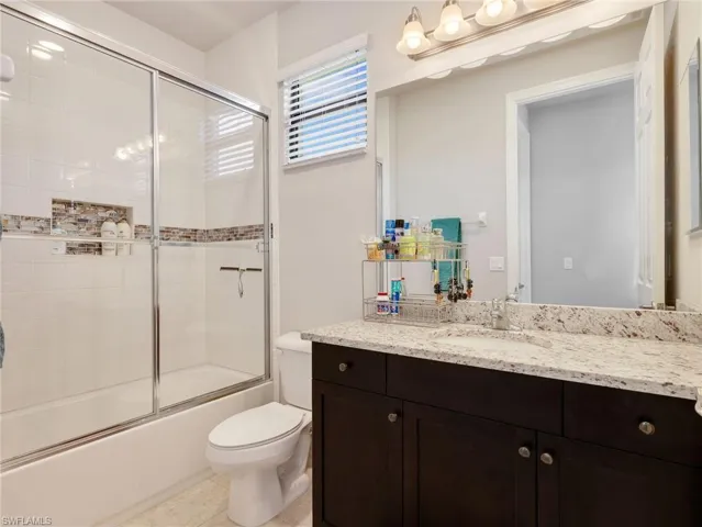 Bathroom featuring a built-in tub with a sliding glass shower door, a tile surround with decorative accent banding, and a recessed niche
