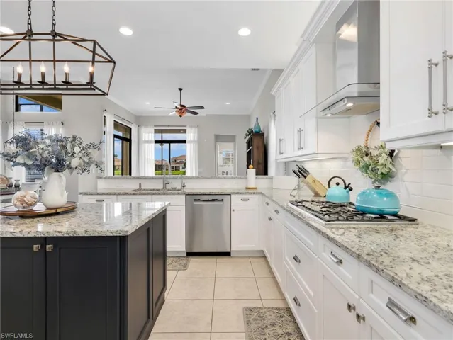 Gourmet kitchen featuring a central island with dark cabinetry, granite countertops, tile flooring, white shaker cabinets, and stainless steel appliances including a gas range and dishwasher