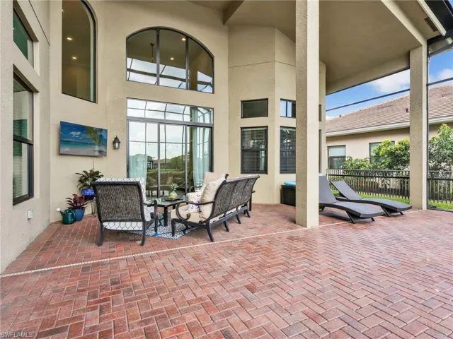 Expansive covered patio featuring herringbone-pattern brick flooring, large arched windows, multiple sets of sliding glass doors, and screened enclosures
