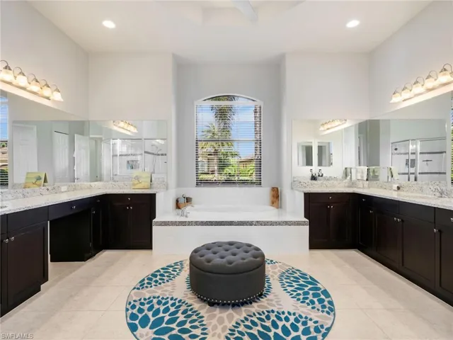 Spacious Master bathroom featuring a built-in soaking tub, dual vanities with stone countertops, dark wood-finish cabinetry, and tile flooring