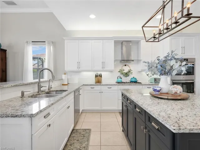 Kitchen featuring white shaker cabinetry, granite countertops, tile flooring, stainless steel appliances, and a central island with dark cabinetry