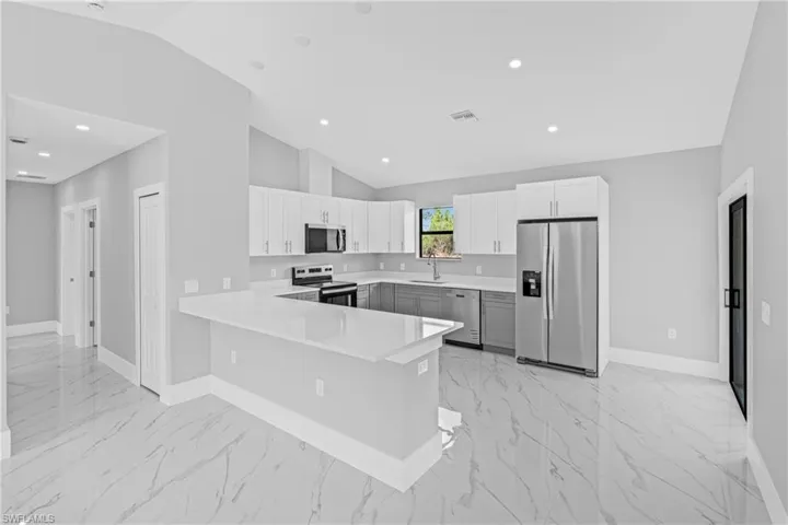 Kitchen with appliances with stainless steel finishes, light marble finish floors, light countertops, vaulted ceiling, and a peninsula