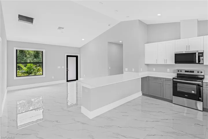 Kitchen with light marble finish floors, appliances with stainless steel finishes, vaulted ceiling, light countertops, and a peninsula