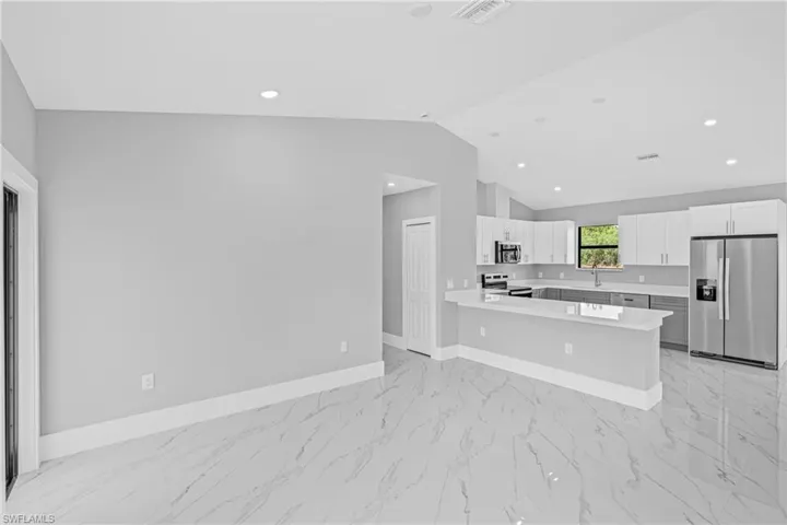 Kitchen with stainless steel appliances, light marble finish floors, light countertops, a peninsula, and vaulted ceiling