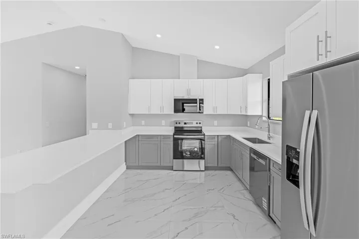 Kitchen with stainless steel appliances, vaulted ceiling, gray cabinets, light marble finish floors, and a peninsula