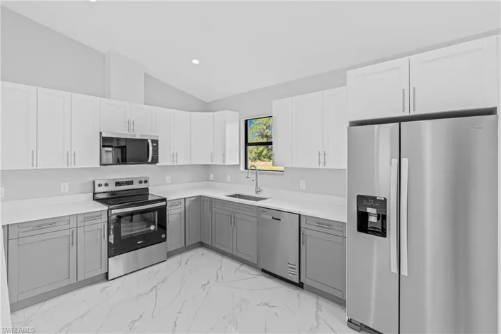 Kitchen with appliances with stainless steel finishes, gray cabinets, vaulted ceiling, light marble finish floors, and light countertops