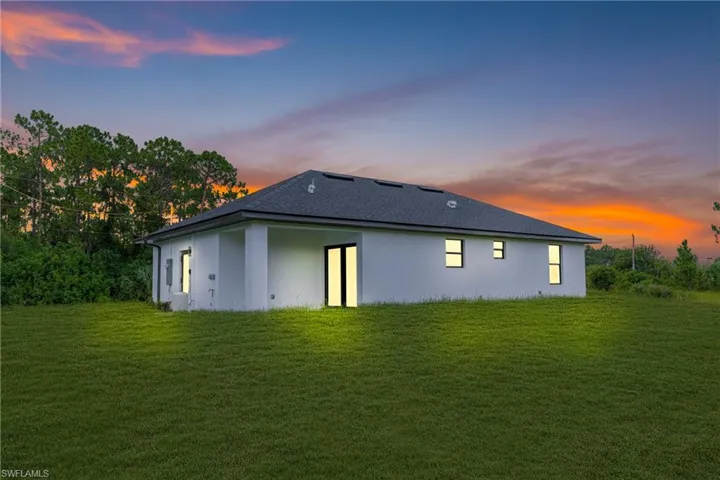 Rear view of property featuring a lawn and stucco siding