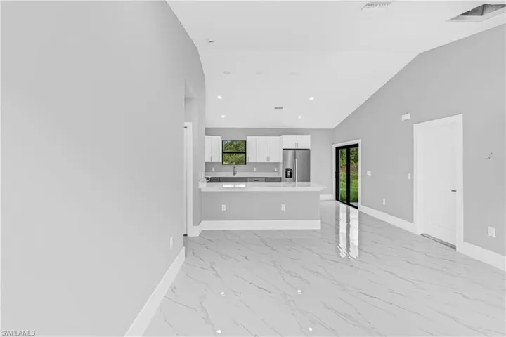 Unfurnished living room featuring light marble finish flooring, plenty of natural light, recessed lighting, and high vaulted ceiling