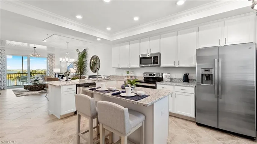 Kitchen with stainless steel appliances, a peninsula, a raised ceiling, white cabinets, and a kitchen island
