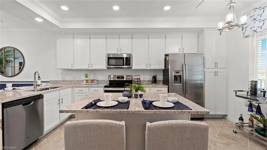 Kitchen with appliances with stainless steel finishes, white cabinetry, ornamental molding, a center island, and light tile patterned floors