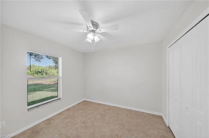 Room featuring neutral wall tones, tile flooring, a window with horizontal blinds, a white ceiling fan with integrated lighting, and bi-fold closet doors