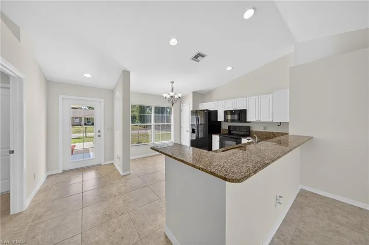 Open-concept living area featuring a kitchen with a raised breakfast bar, granite countertops, white cabinetry, and black appliances