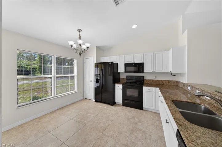 Bright kitchen featuring white cabinetry, black appliances, a double basin sink, and granite countertops