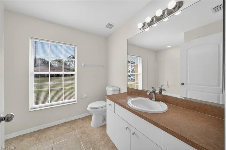 Bathroom featuring a single vanity with a brown countertop, an integrated oval sink, and a large wall-mounted mirror