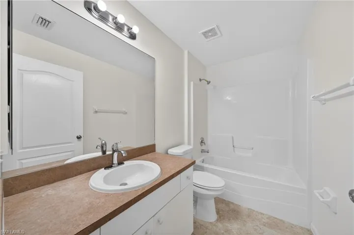 Bathroom featuring a single vanity with a laminate countertop, an integrated sink, a large wall-mounted mirror, and a combined shower-tub unit