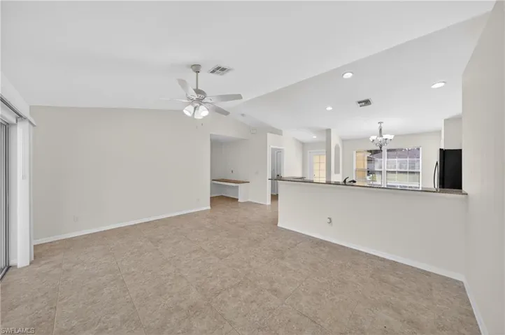 Open-concept living area featuring a kitchen with a raised breakfast bar, granite countertops, white cabinetry, and black appliances