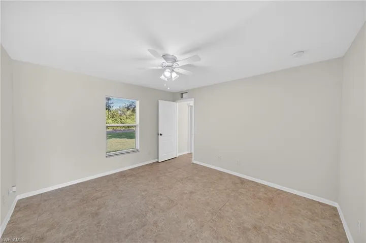 Spacious room featuring tile flooring, neutral wall tones, a ceiling fan with integrated lighting, and a window providing natural light and exterior scenery