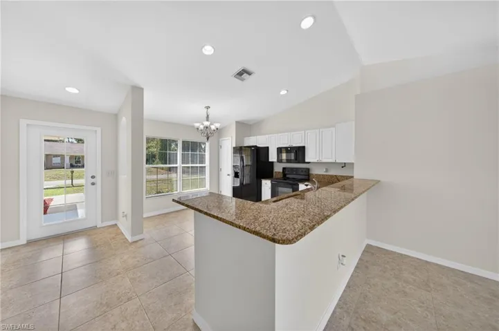 Kitchen featuring a breakfast bar with stone-finish countertop, white cabinetry, and black appliances