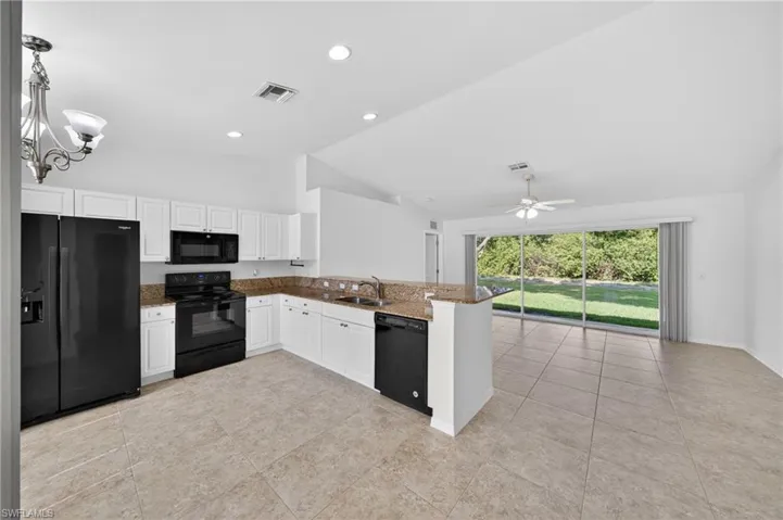 Open-concept kitchen featuring white cabinetry, black appliances, recessed lighting, and a breakfast bar