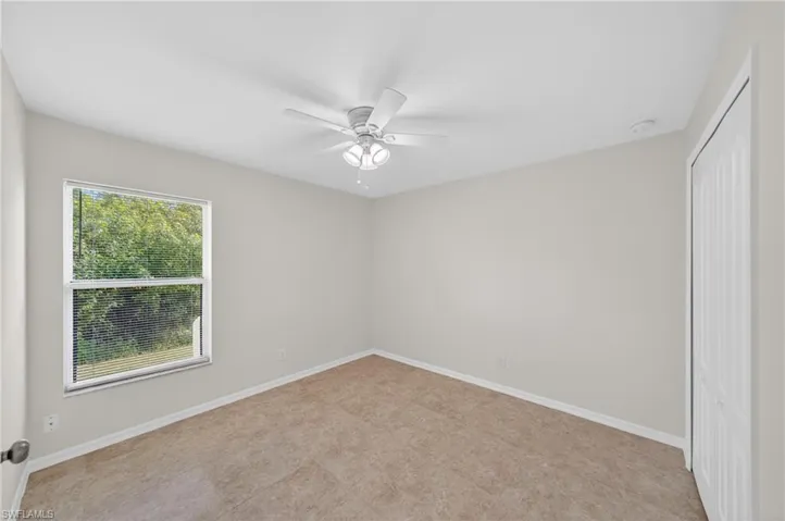 Spacious room with light neutral walls, textured carpeting, a ceiling fan with integrated lighting, a large window with blinds, and a bi-fold closet door