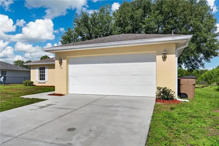 Cream-colored stucco exterior featuring a prominent white garage door, concrete driveway, and a white shuttered window