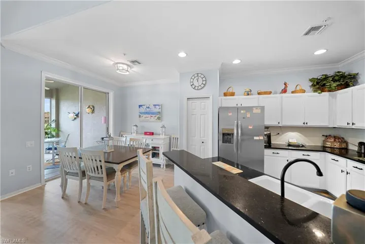 Kitchen featuring stainless steel refrigerator with ice dispenser, crown molding, white cabinets, light wood-style flooring, and dark stone countertops