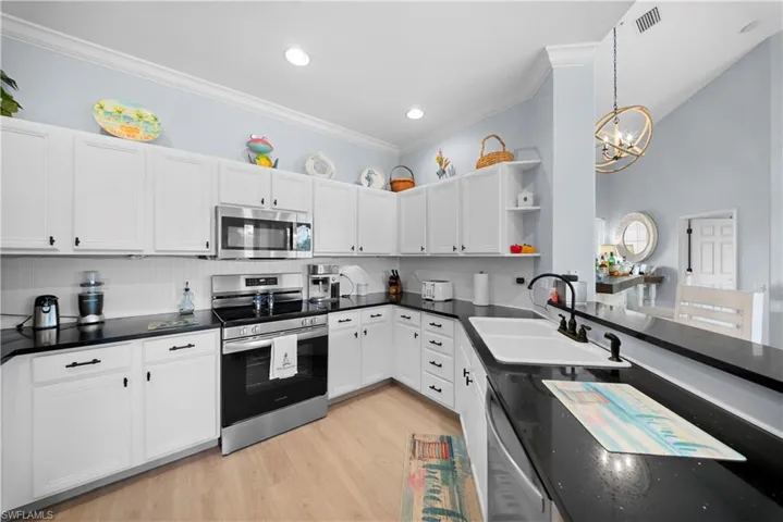 Kitchen with stainless steel appliances, white cabinets, ornamental molding, open shelves, and light wood-type flooring