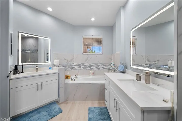 Bathroom featuring two vanities, light wood-style floors, a garden tub, and a marble finish shower