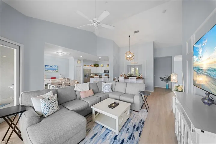 Living room with light wood-type flooring, a ceiling fan, a chandelier, and lofted ceiling