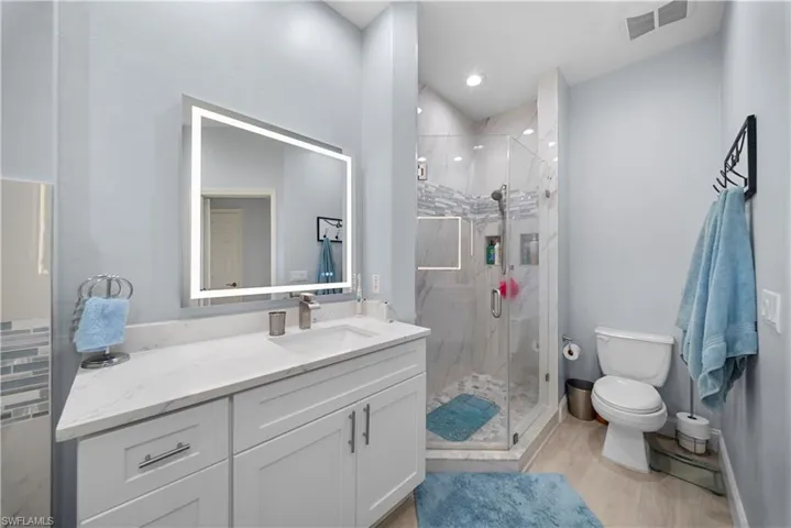 Full bathroom with vanity, a marble finish shower, light wood-type flooring, and recessed lighting