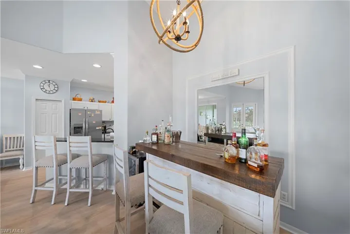 Bar area featuring stainless steel fridge with ice dispenser, a high ceiling, white cabinetry, light wood-style floors, and hanging lights