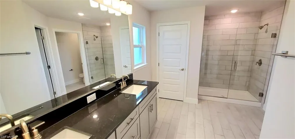 Bathroom featuring toilet, hardwood / wood-style flooring, an enclosed shower, and double vanity