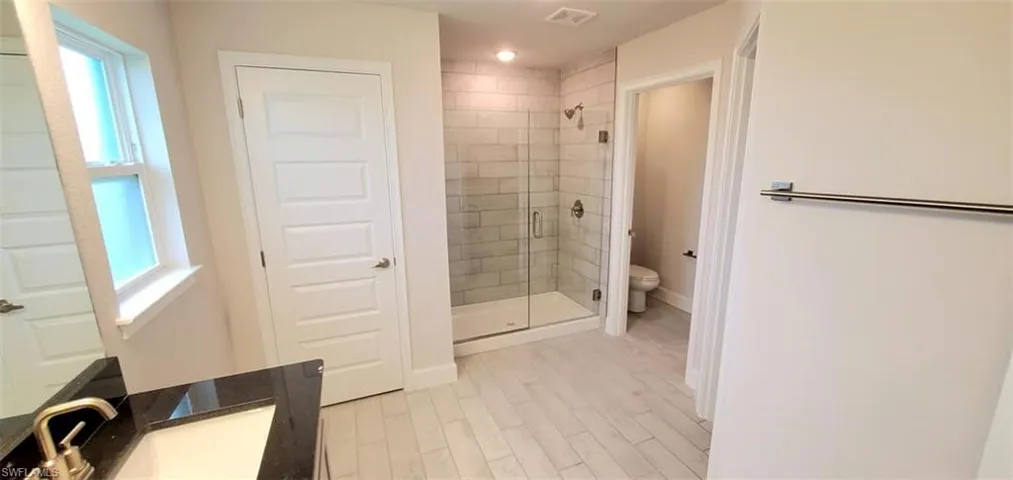 Bathroom featuring hardwood / wood-style floors, toilet, an enclosed shower, and plenty of natural light